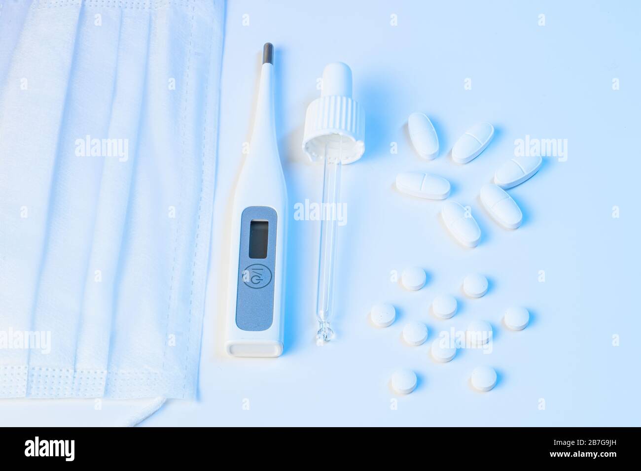 thermomètre électronique, masque de protection, pilules pour pipettes et comprimés se trouvent sur un fond blanc avec un éclairage bleu Banque D'Images