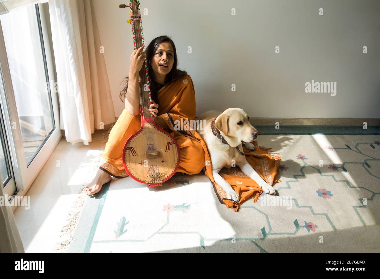 Femme assise avec son chien par son côté et jouant de la musique sur son tambra. Banque D'Images