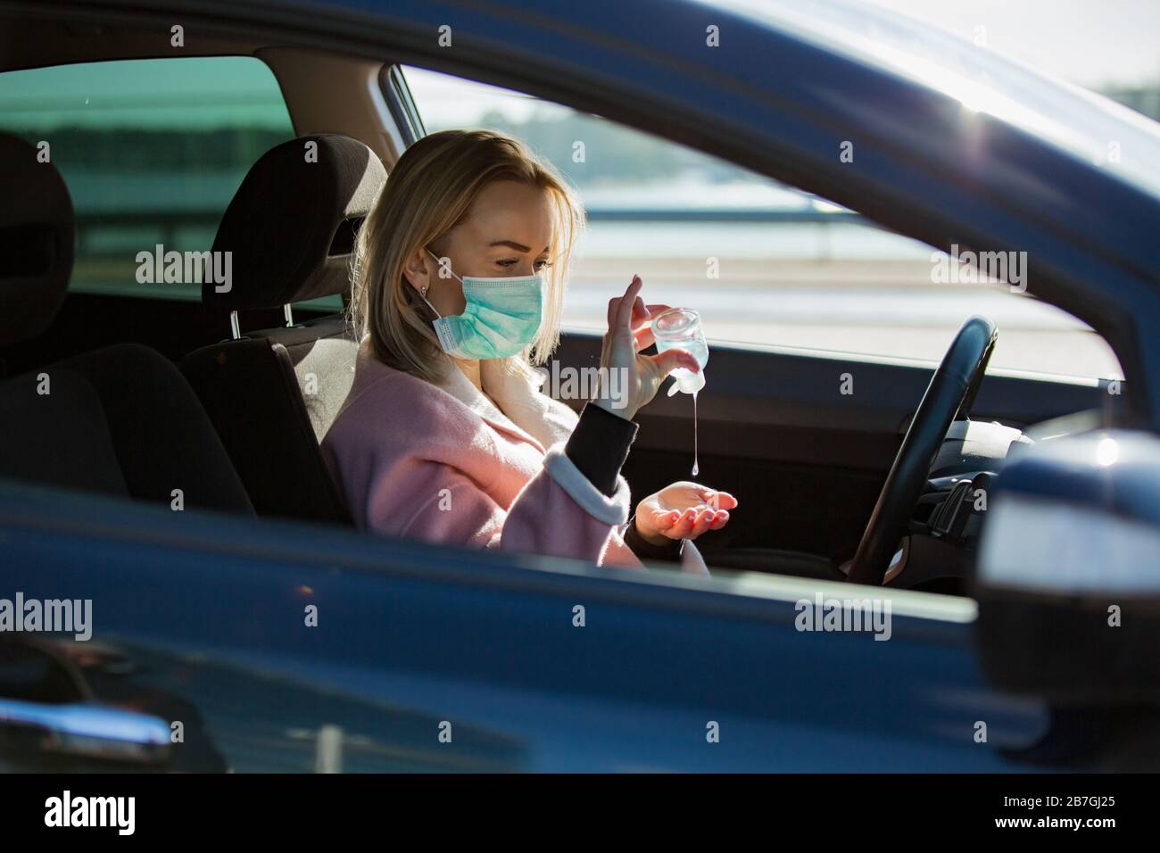 Femme dans un masque de protection assis dans une voiture sur la route, à l'aide d'un désinfectant pour les mains. Transport en toute sécurité. Banque D'Images
