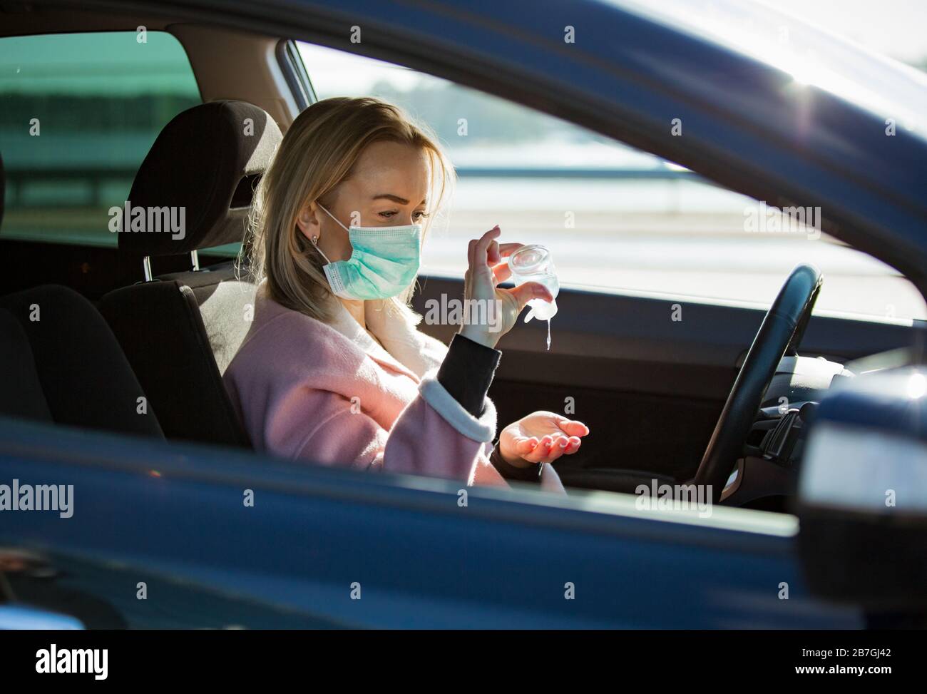 Femme dans un masque de protection assis dans une voiture sur la route, à l'aide d'un désinfectant pour les mains. Transport en toute sécurité. Banque D'Images