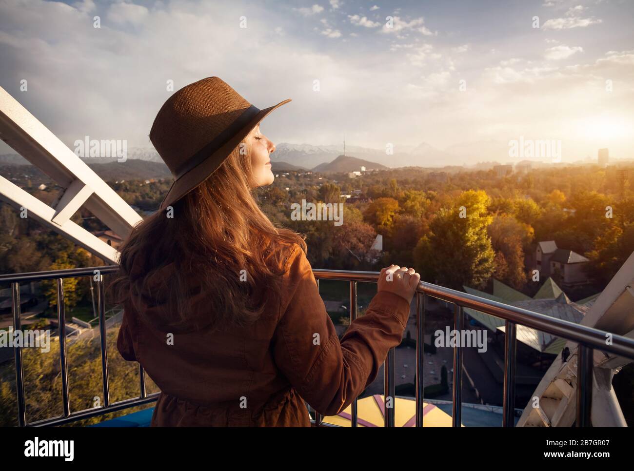 Femme avec chapeau à la cabine de la grande roue dans le parc de l'automne au coucher du soleil Banque D'Images