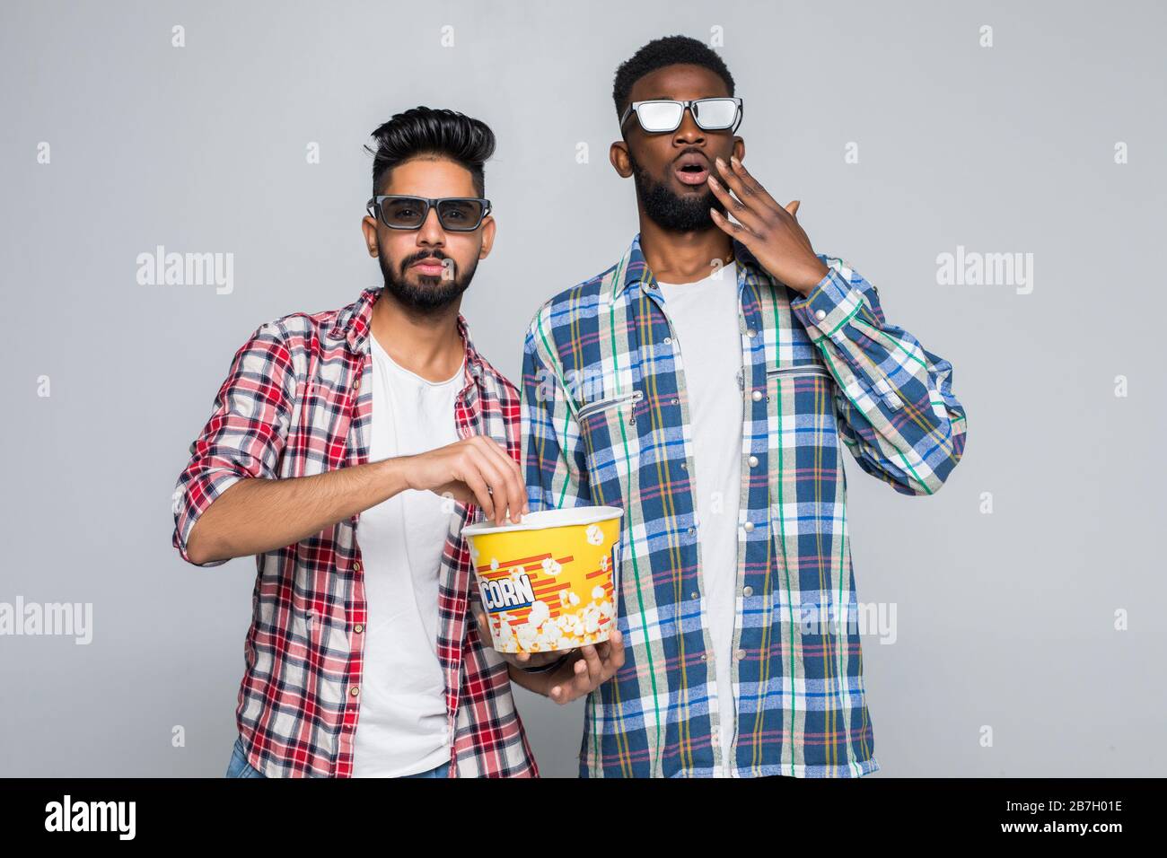Deux hommes de course mixtes portent des lunettes en relief et mangent du pop-corn sur fond gris Banque D'Images