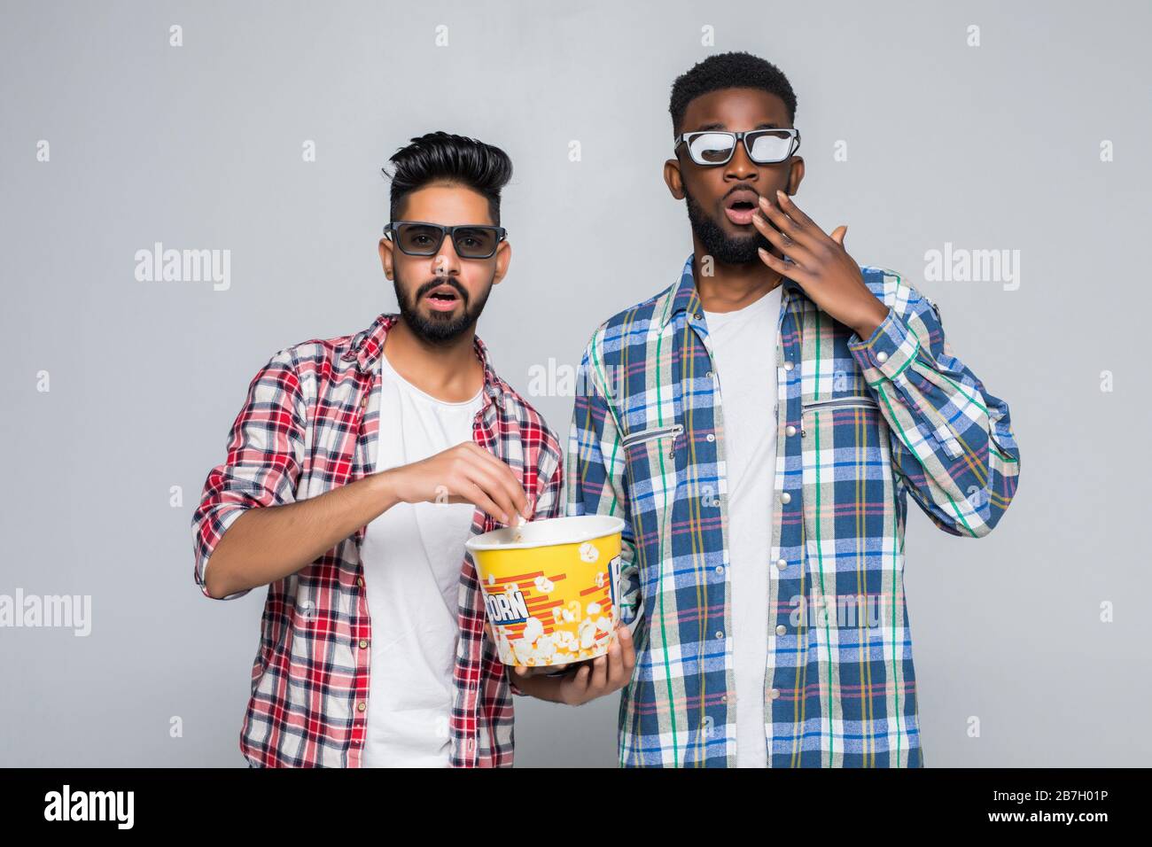 Deux hommes de course mixtes portent des lunettes en relief et mangent du pop-corn sur fond gris Banque D'Images