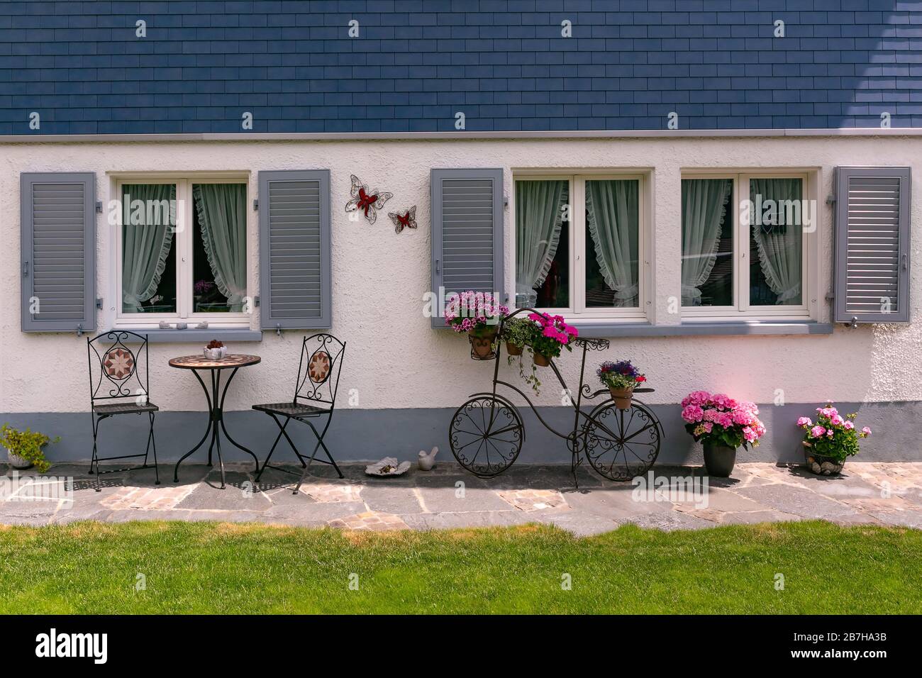 Façade d'une maison suisse moderne avec coin salon et pots de fleurs, vélo décoratif forgé dans les Alpes suisses, Suisse. Banque D'Images