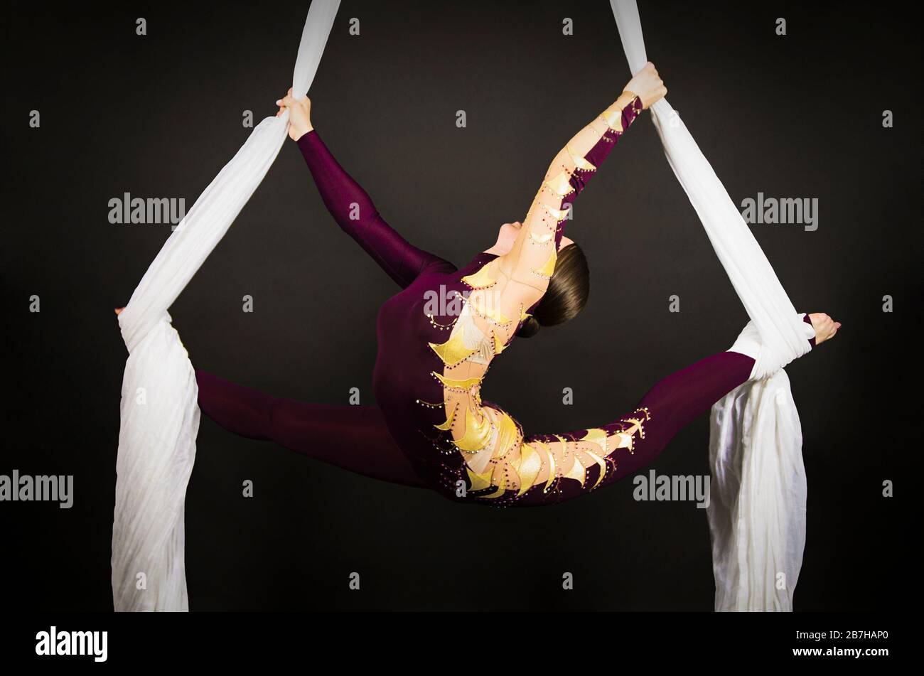 Femme sportive en costume de Bourgogne effectuant des exercices de gymnastique et de cirque sur de la soie blanche. Prise de vue en studio sur fond sombre, images isolées. Banque D'Images