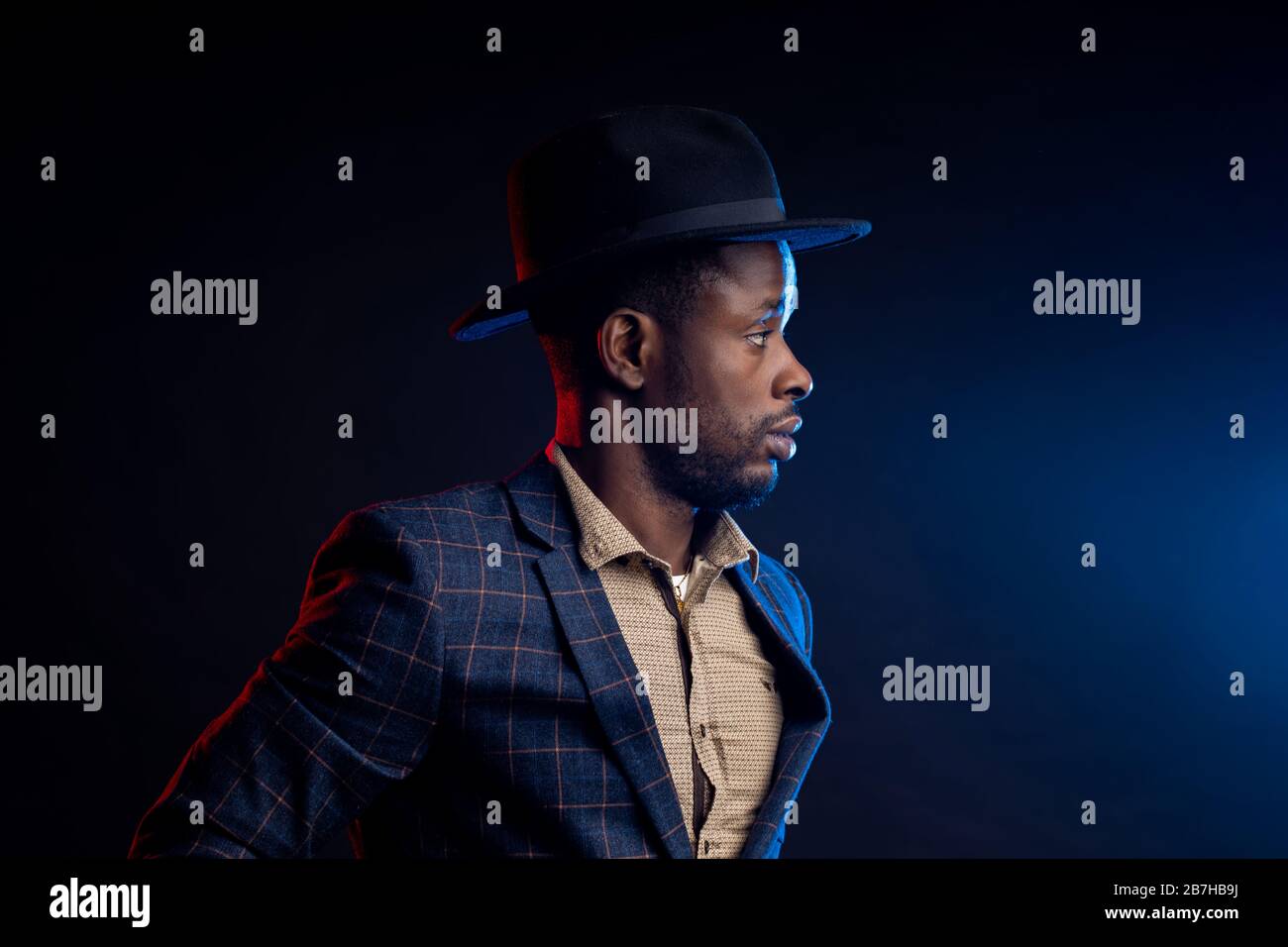 Portrait studio taille haute de jeune homme d'affaires africain peu rasé, confiant et sérieux, portant une chemise, costume à damier debout contre le noirceur Banque D'Images