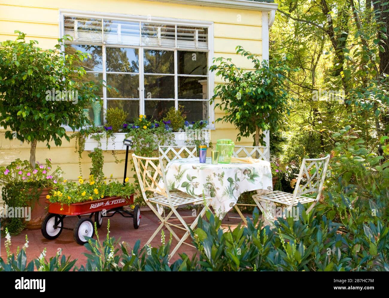 Porche avant avec table de café blanche et chaises, chariot rouge avec fleurs Banque D'Images
