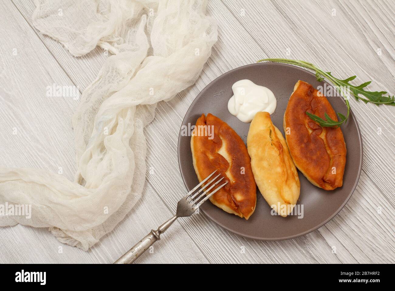 Plaque avec tartes fries, crème aigre et fourchette, gaze blanche sur planches en bois. Vue de dessus. Banque D'Images