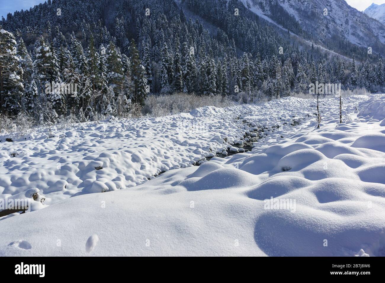 Séchez la rivière Amanauz traverse les pierres enneigées du village de Dombay. Pentes de montagne surcultivées avec forêt de sapin Banque D'Images