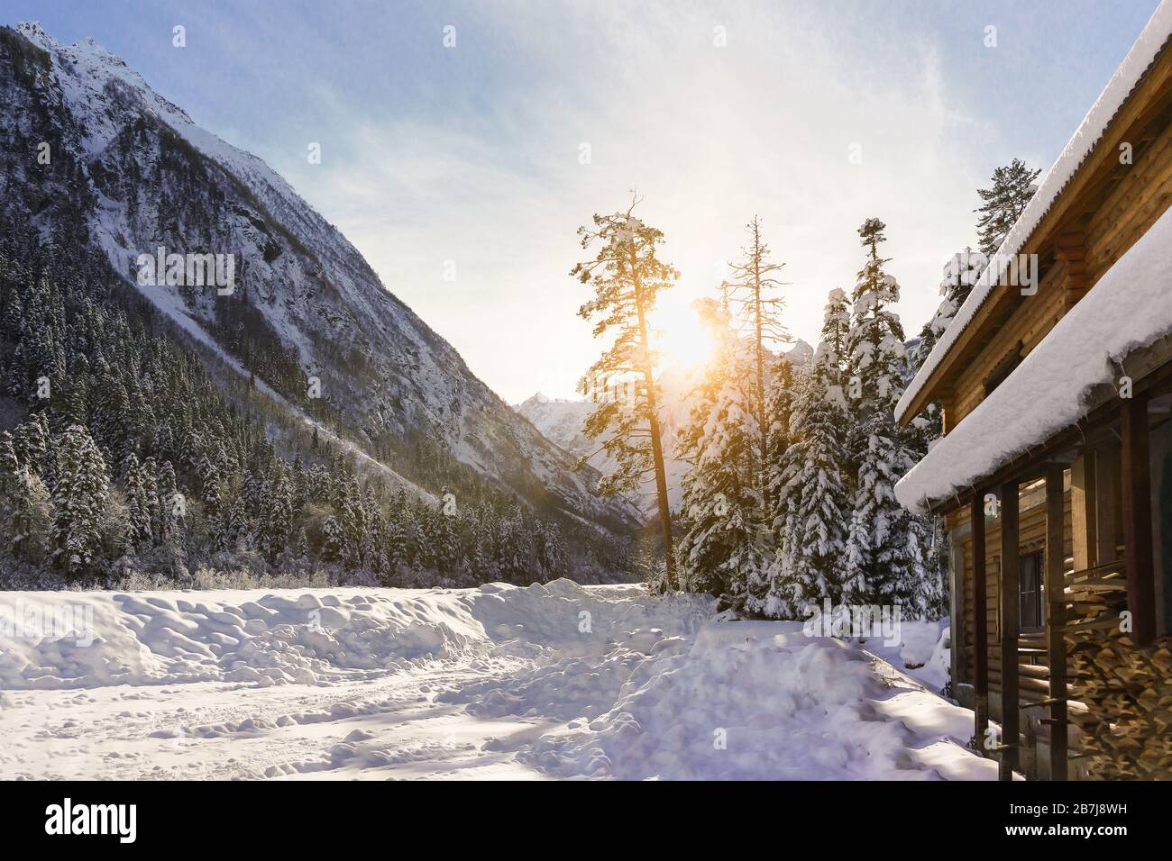 Les rayons du soleil de derrière la montagne illuminent une maison en bois à la périphérie du village de Dombay. Aube d'hiver à la station de ski Banque D'Images