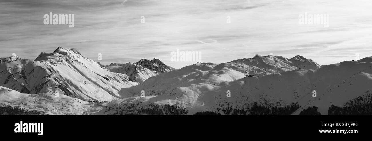 Panorama des pentes enneigées dans les montagnes d'hiver et ciel nuageux ensoleillé en soirée. Alpes italiennes. Livigno, région de Lombardie, Italie, Europe. Noir et Banque D'Images