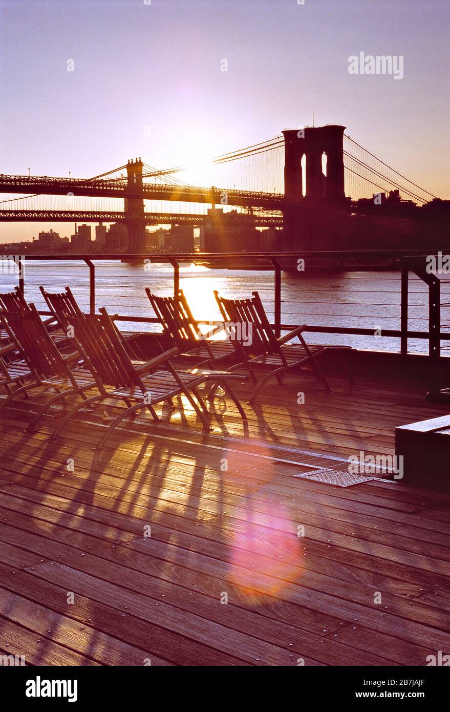 ÉTATS-UNIS. New York. Pont de Brooklyn sur la vue du lever du soleil sur East River depuis la promenade avec chaises longues. Banque D'Images