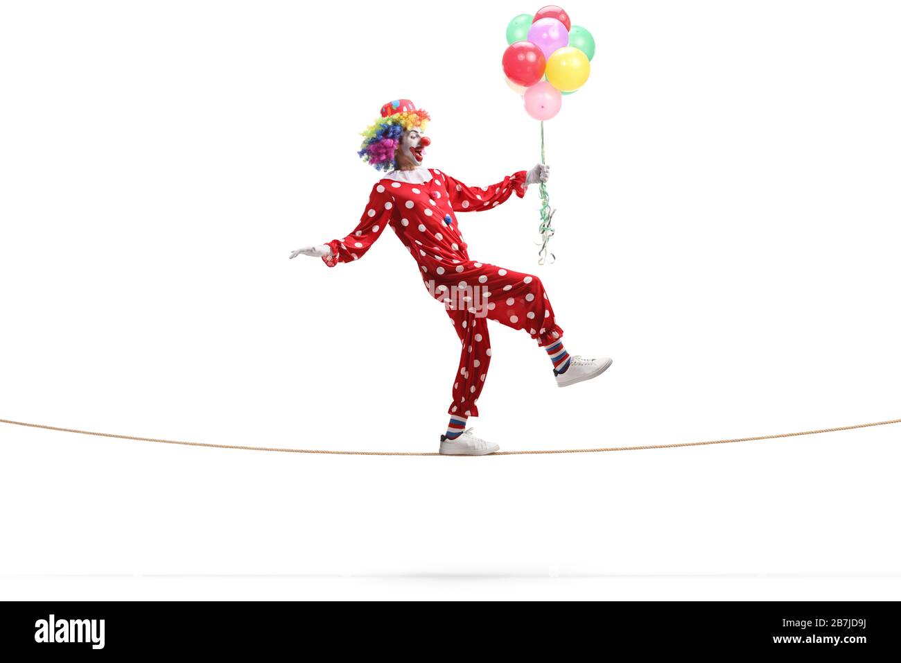 Profil de pleine longueur tiré d'une clown marchant sur une corde et tenant une bande de ballons isolés sur fond blanc Banque D'Images