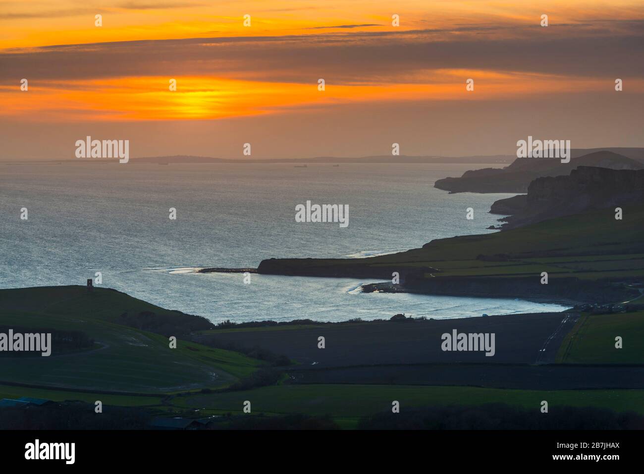 Kimmeridge, Dorset, Royaume-Uni. 16 mars 2020. Météo britannique. Le ciel s'illumine d'orange au coucher du soleil, vu de Swyre Head près de Kimmeridge sur la côte jurassique de Dorset en direction de l'ouest sur Kimmeridge Bay et Warbarrow Bay après une journée de soleil chaud et de ciel bleu clair. Crédit photo : Graham Hunt/Alay Live News Banque D'Images