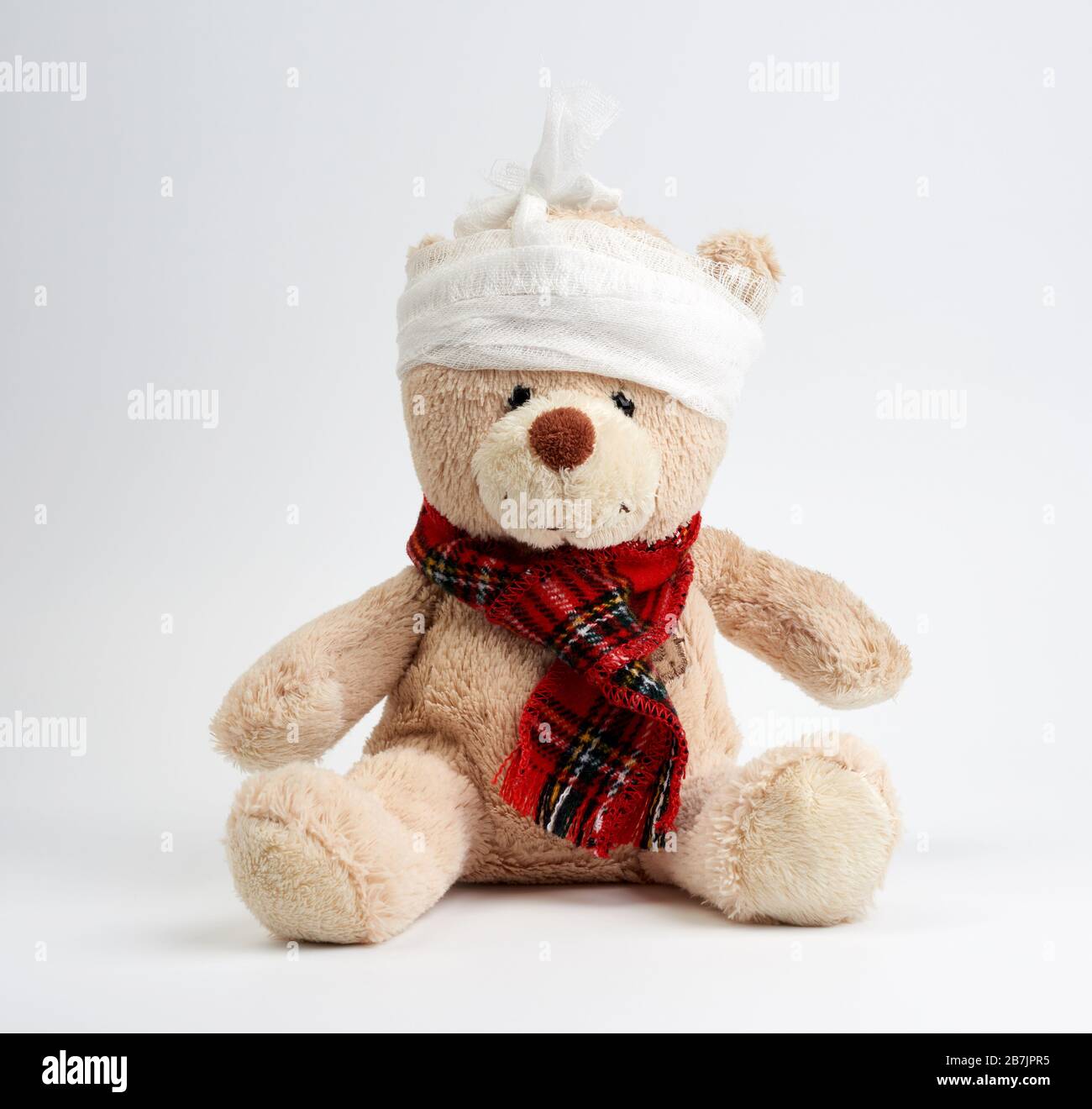 grand ours en peluche avec une tête bandée dans un bandage médical blanc sur un fond blanc, concept de traumatisme d'enfant, maux de tête Banque D'Images