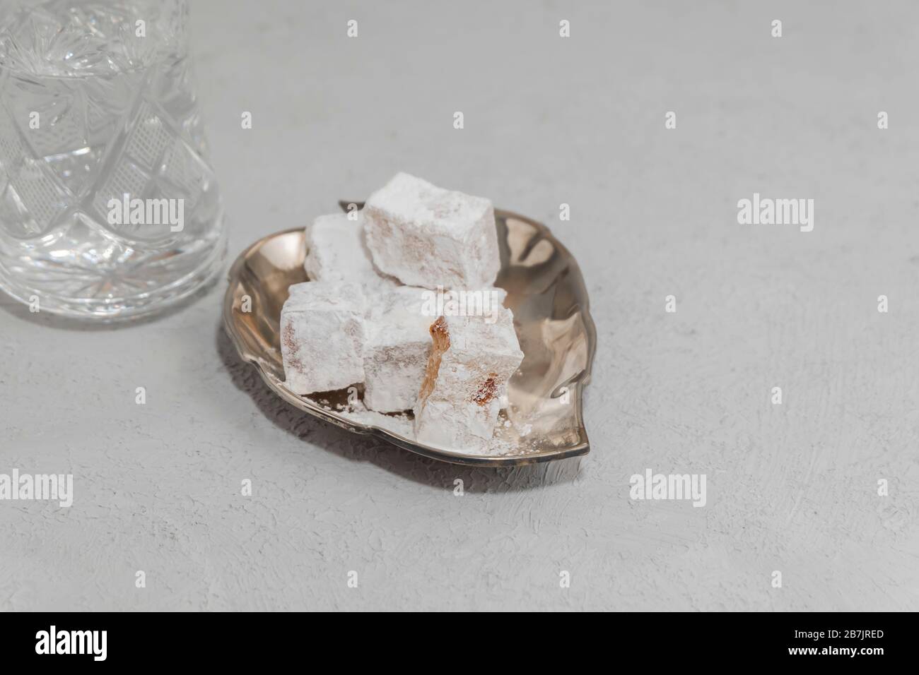 Lokum en plaque métallique avec verre d'eau sur fond de béton. Une cuisine douce pour le Ramadan Banque D'Images