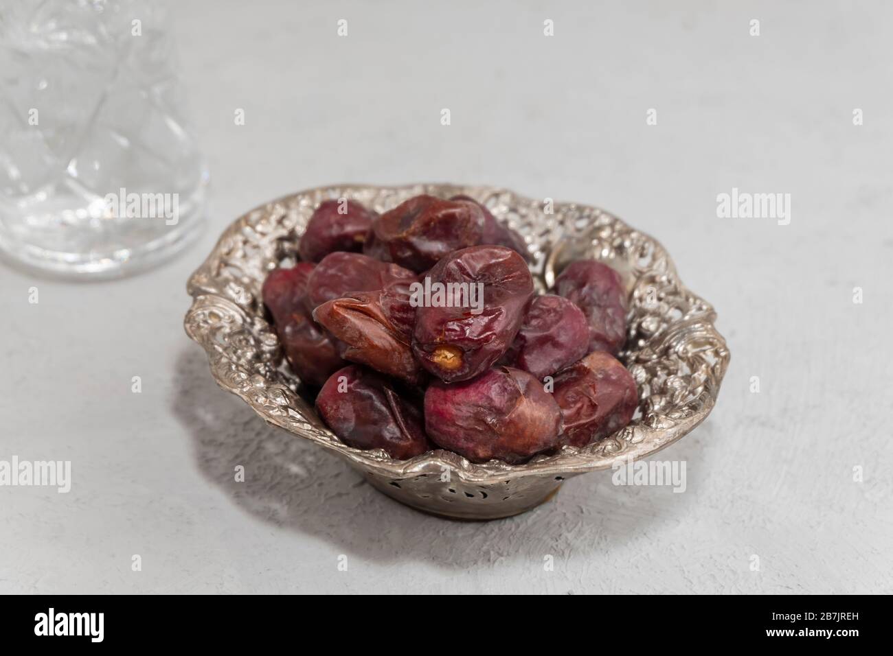 Gros plan des dates sèches dans une plaque métallique avec verre d'eau sur fond en béton neutre. Concept de jeûne du Ramadan Banque D'Images