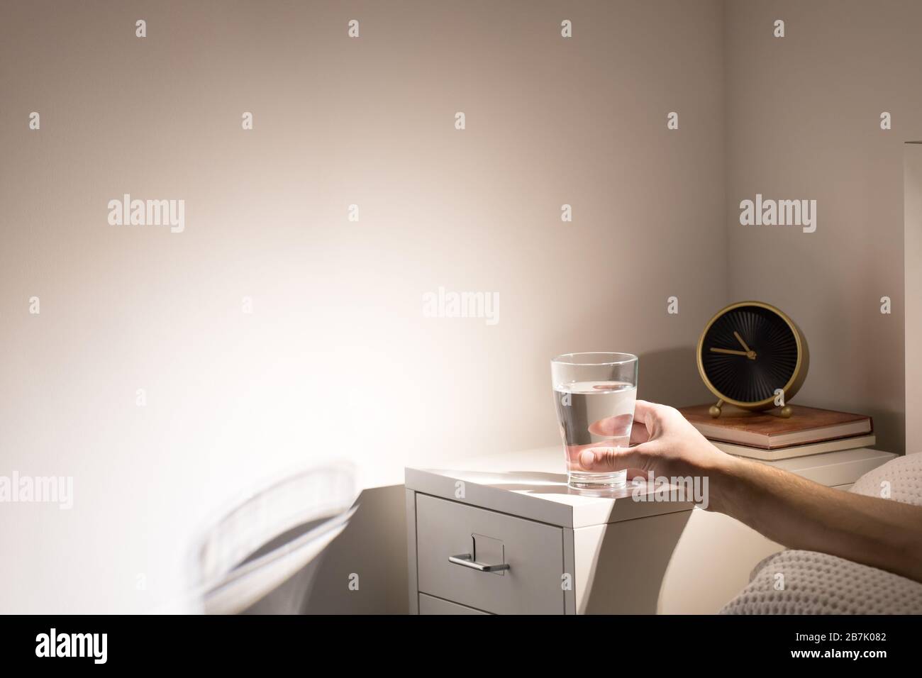Bonne habitude - boire un verre d'eau avant d'aller dormir. Homme au lit prenant un verre d'eau de la table de chevet avant le coucher, copier l'espace. Banque D'Images