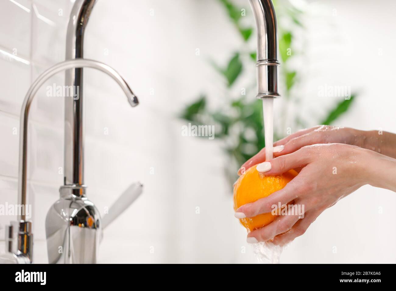 Mains de femme se lavant de l'orange mûr sous le robinet dans la cuisine de l'évier. Banque D'Images