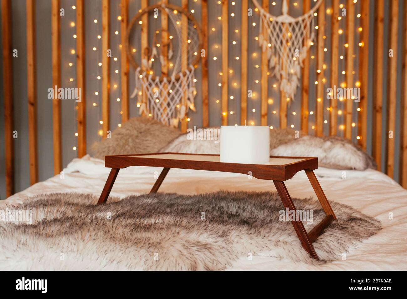 Table en bois vide plateau de petit-déjeuner dans le lit. Chambre Boho, décoration murale en bois avec guirlandes, lampes et trancheuses de rêve. Banque D'Images