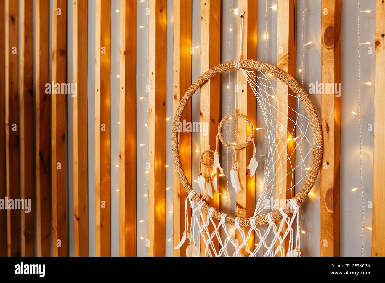 Décoration ethno pour le mur Dreamcatcher de brises, perles et plumes tressées sur un mur en bois avec des guirlandes. Banque D'Images