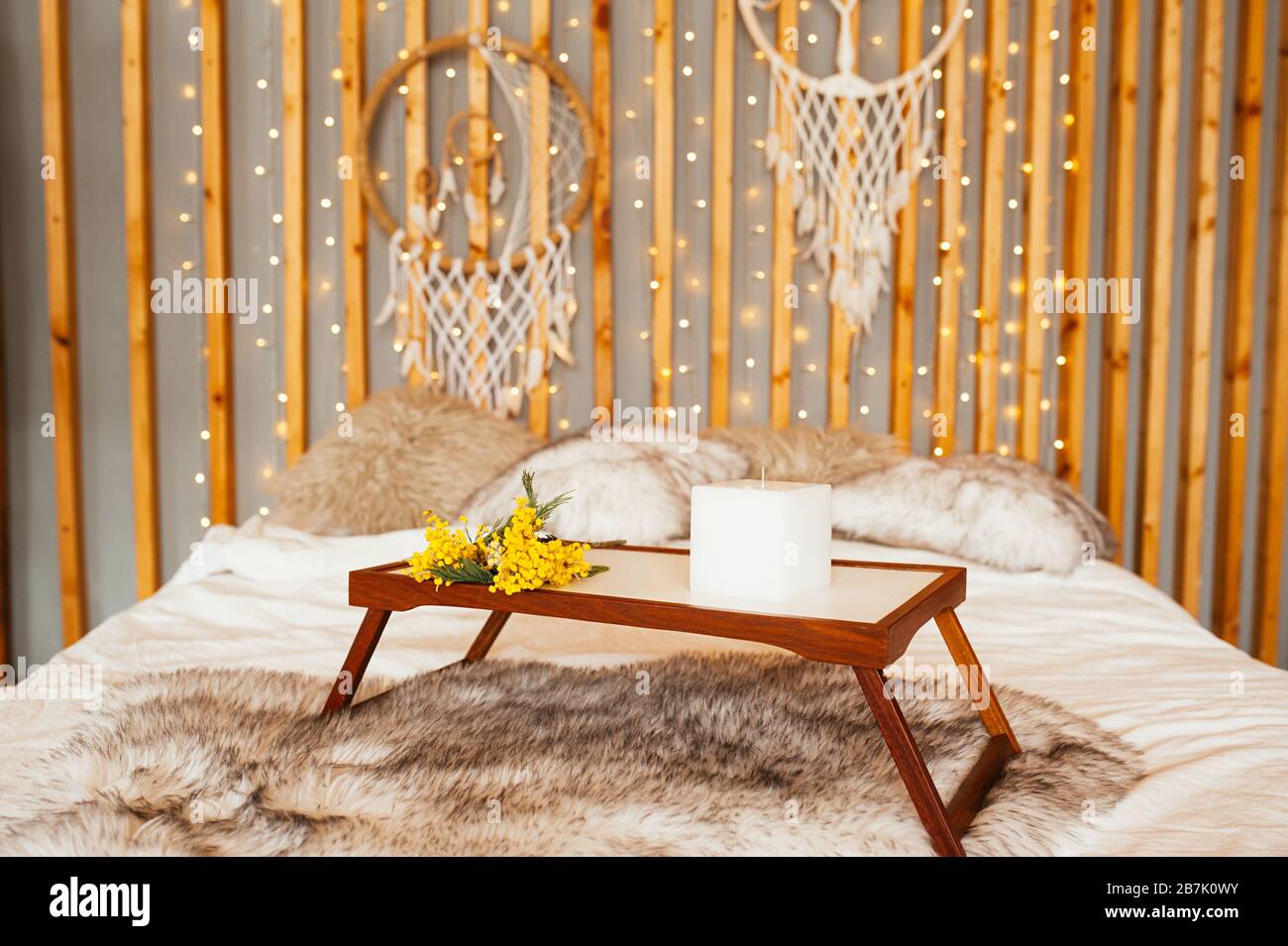 Bouquet jaune Mimosa sur la table en bois, plateau de petit-déjeuner au lit. Chambre Boho, décoration murale en bois avec guirlandes, lampes et trancheuses de rêve. Banque D'Images