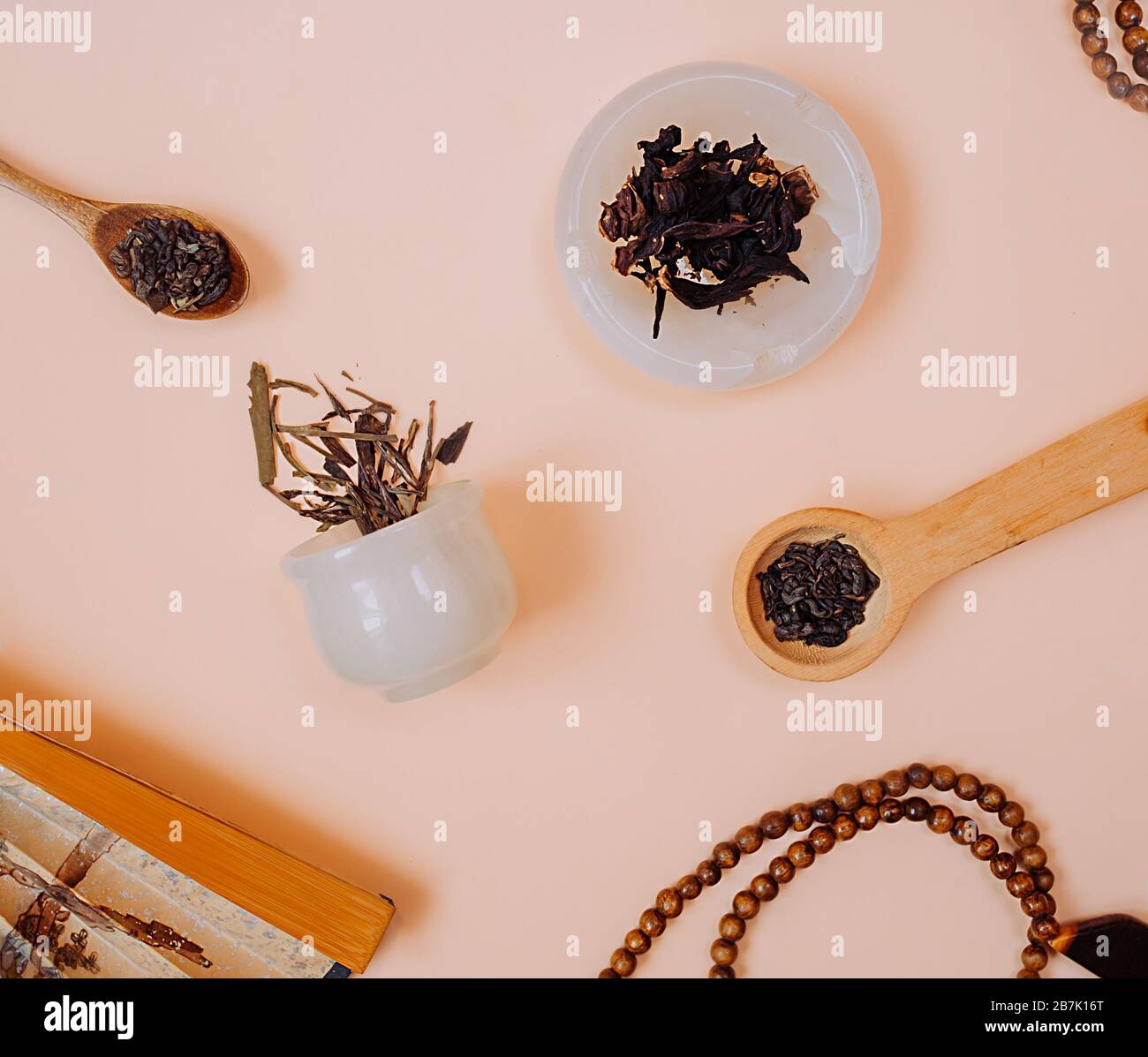 Image carrée d'une fête du thé chinois. Granules secs de différents types de thé dans une tasse de pierre blanche, dans des cuillères en bois sur un fond rose délicat. Retour Banque D'Images