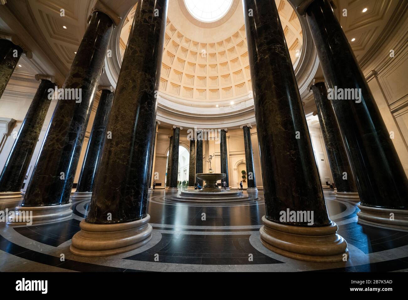 Rotonde de la National Gallery of Art Rotunda Washington DC // WASHINGTON, DC, États-Unis — la grande rotonde de la National Gallery of Art de Washington, DC, présente une architecture néoclassique avec son impressionnant dôme, sa lucarne et ses colonnes corinthiennes. Une fontaine centrale ajoute un élément dynamique à l’espace circulaire, qui sert d’entrée principale et de point focal du musée. La conception de la rotonde, avec une disposition symétrique et des proportions classiques, illustre la vision de l'architecte John Russell Pope. Banque D'Images