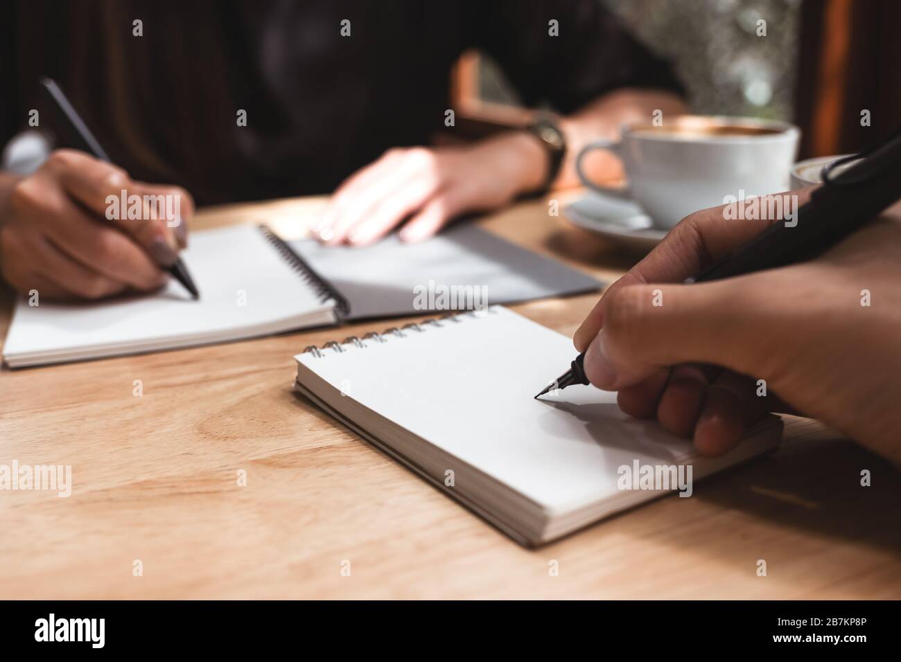 Gros plan image de deux hommes d'affaires écrivant sur un cahier blanc vierge avec une tasse de café sur une table en bois au bureau Banque D'Images