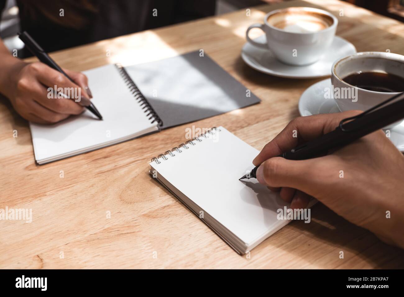 Gros plan image de deux hommes d'affaires écrivant sur un cahier blanc vierge avec une tasse de café sur une table en bois au bureau Banque D'Images