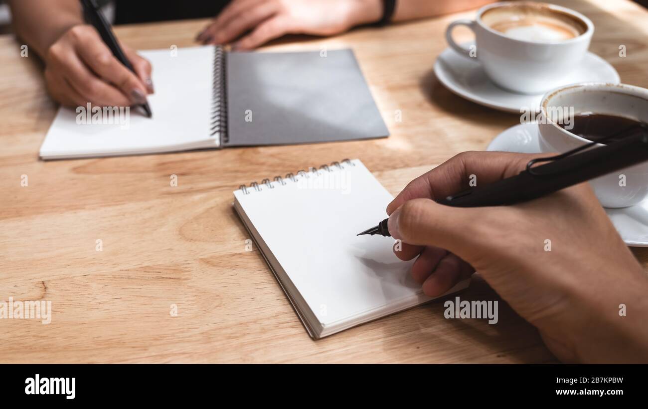 Gros plan image de deux hommes d'affaires écrivant sur un cahier blanc vierge avec une tasse de café sur une table en bois au bureau Banque D'Images