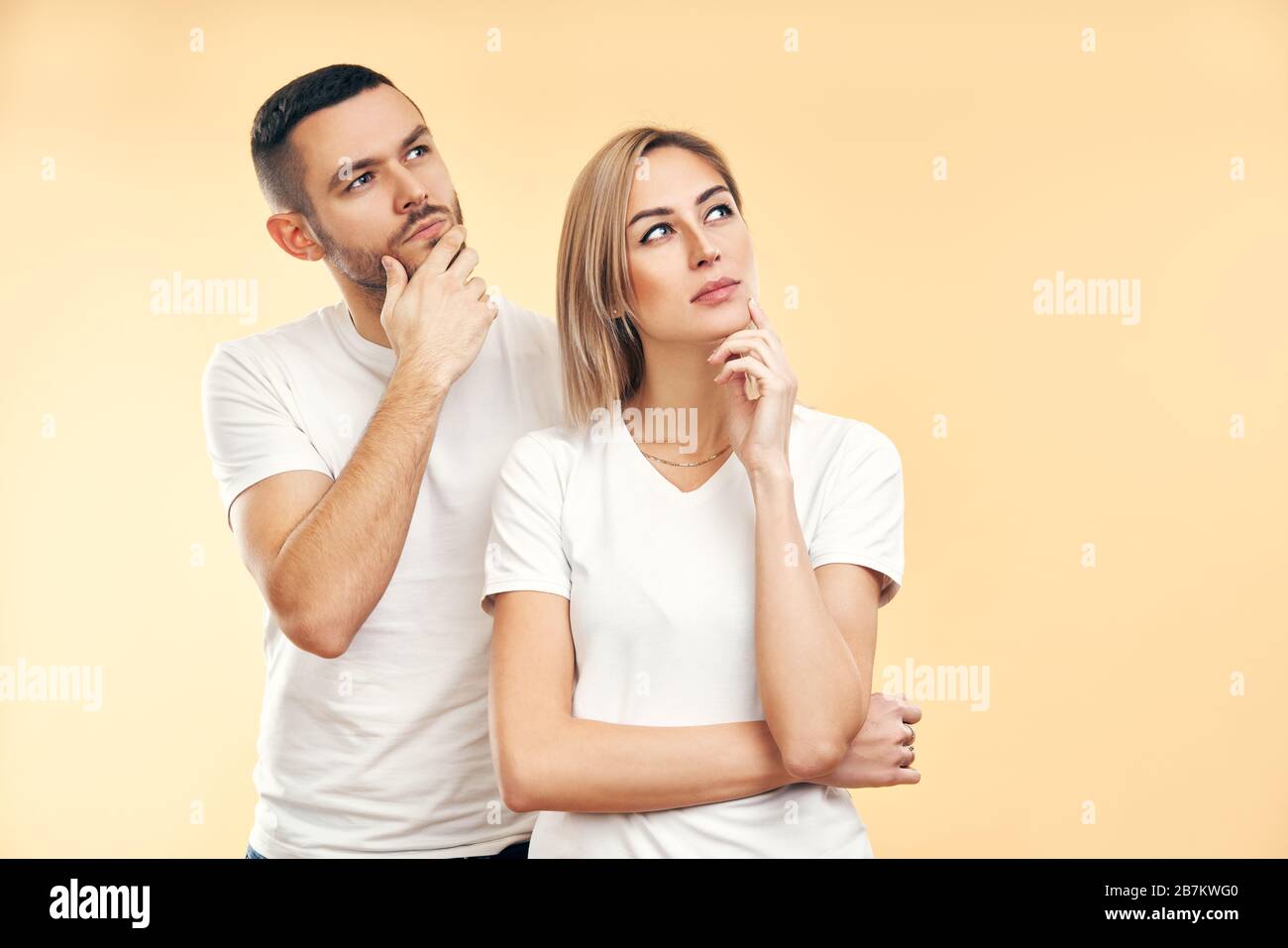 Jeune homme et femme pendus regardant latéralement isolé sur fond beige. Doute, concept d'intérêt Banque D'Images