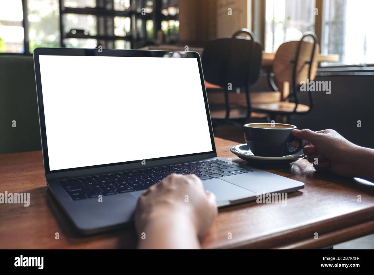 Immersive image d'une femme à l'aide d'un ordinateur portable avec écran de  bureau blanc à blanc tout en buvant un café chaud sur la table en bois dans  la région de cafe