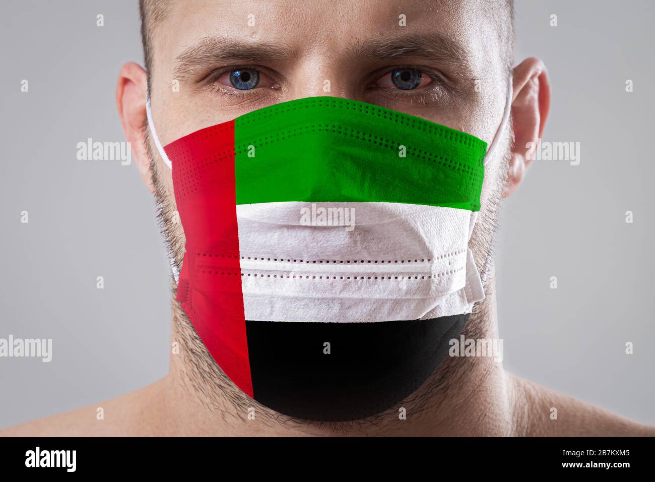 Jeune homme aux yeux douloureux dans un masque médical peint dans les couleurs du drapeau national des Émirats arabes Unis. Protection médicale contre le dis Banque D'Images