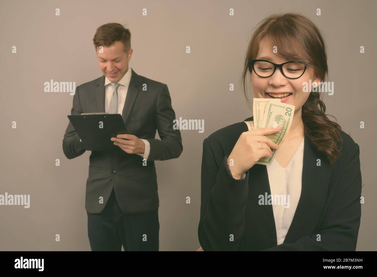 Studio shot of young handsome businessman et jeune belle Asian businesswoman wearing eyeglasses contre l'arrière-plan gris Banque D'Images