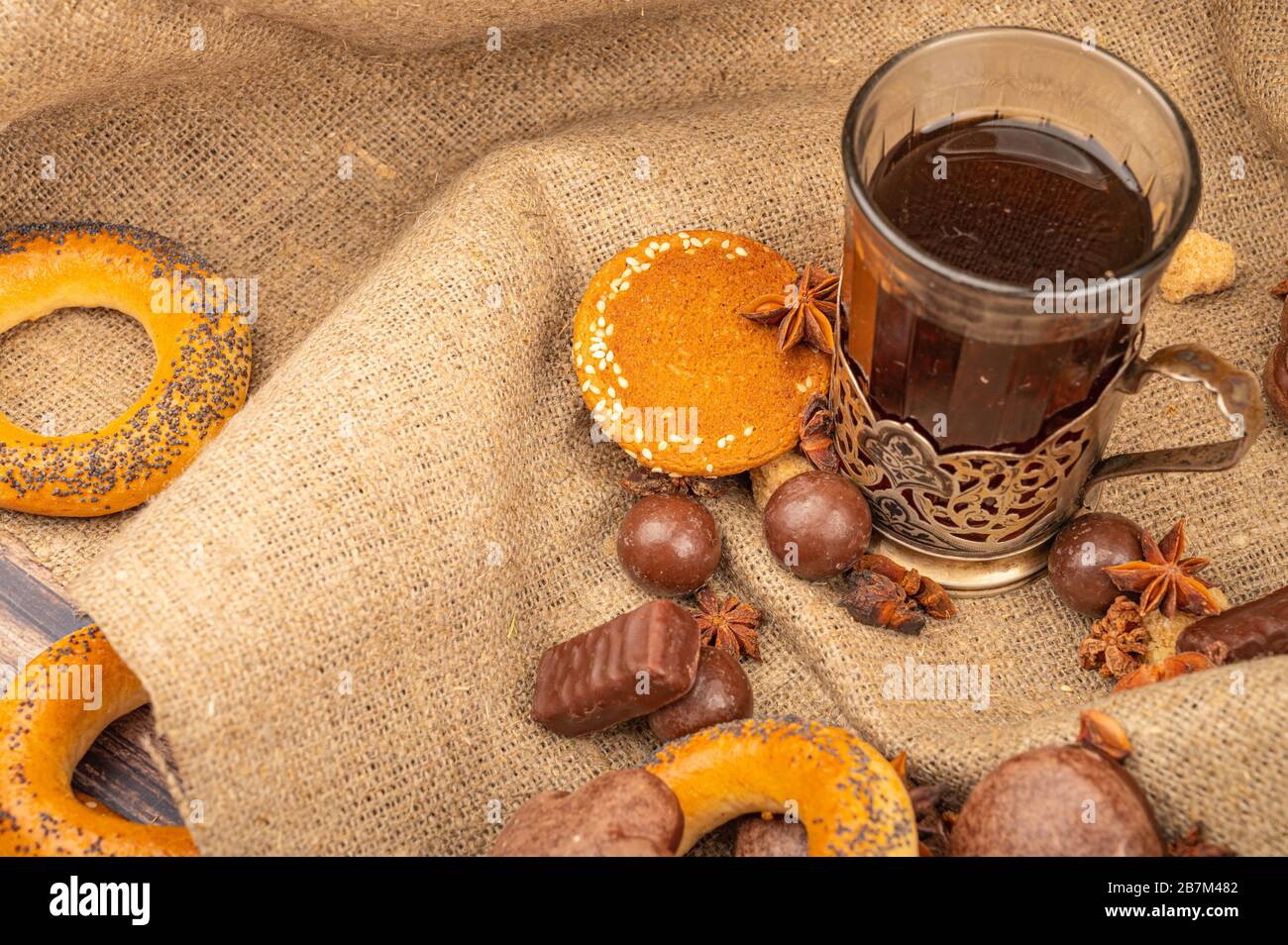 Un verre à facettes de thé dans un porte-gobelet millésime , chocolat, bagels et pain d'épices au chocolat sur fond de tissu grossier. Gros plan Banque D'Images