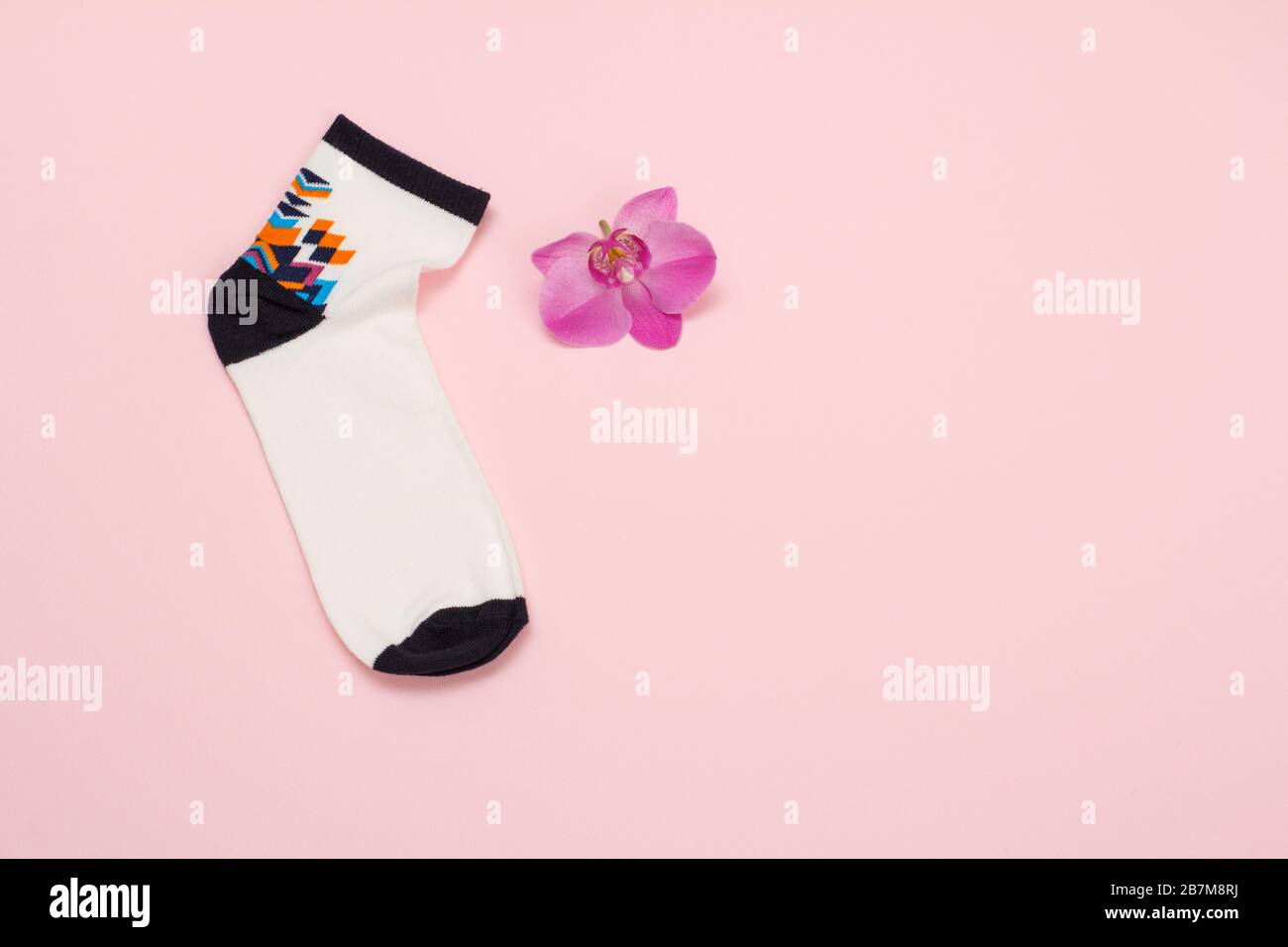 Une chaussette blanche et noire pour femme et une fleur d'orchidée sur fond rose, vue du dessus avec espace de copie. Banque D'Images