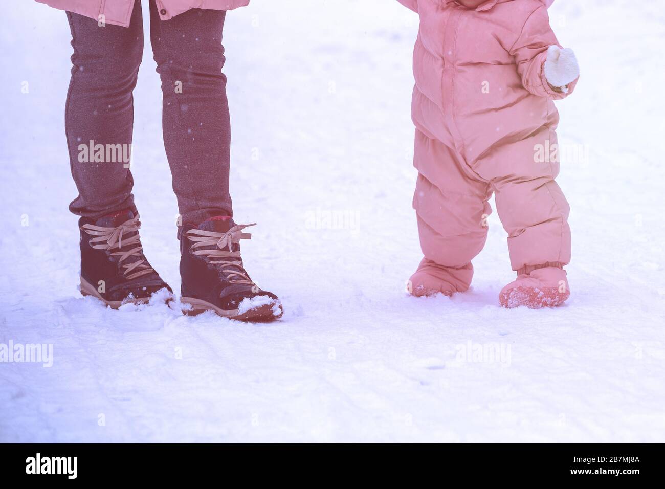 Premières étapes. La maman tient le bébé à la main. Maman et petite fille marchent dans la neige en hiver. L'enfant prend ses premiers pas à l'extérieur dans la neige Banque D'Images