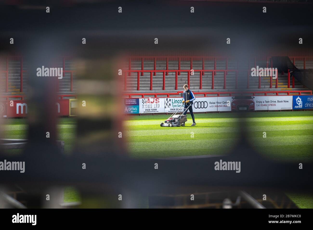 Groundsman travaillant au terrain de football coupant l'herbe, photographié à travers l'écart dans l'obturateur fermé. Banque D'Images