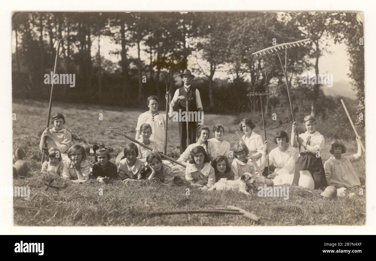 Carte postale des écolières du début des années 1900 lors d'une excursion d'une journée dans le pays, posant avec un agriculteur et des râteaux, vers 1923, Royaume-Uni Banque D'Images