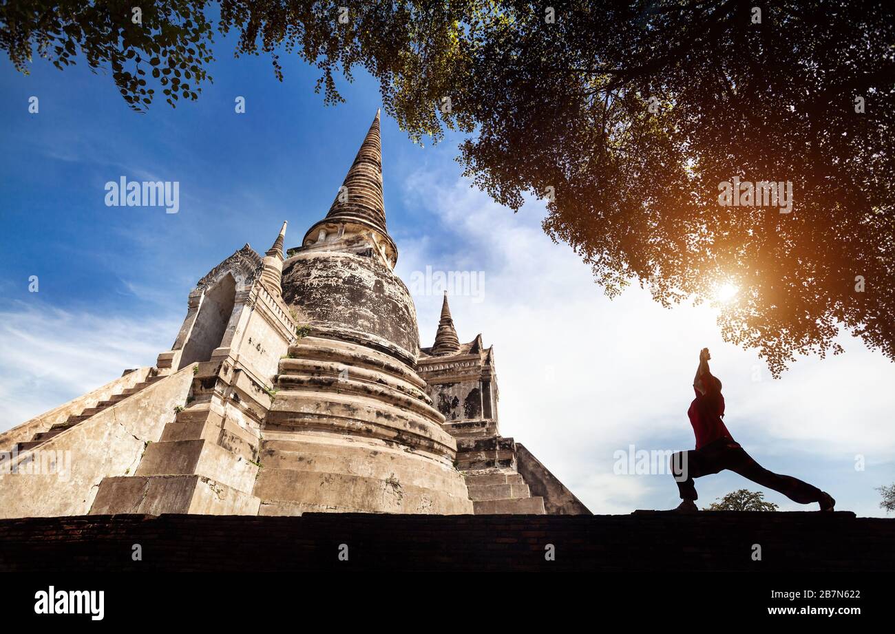 Woman doing Yoga guerrier poser près de temple historique en silhouette dans le parc historique d'Ayutthaya, Thaïlande Banque D'Images