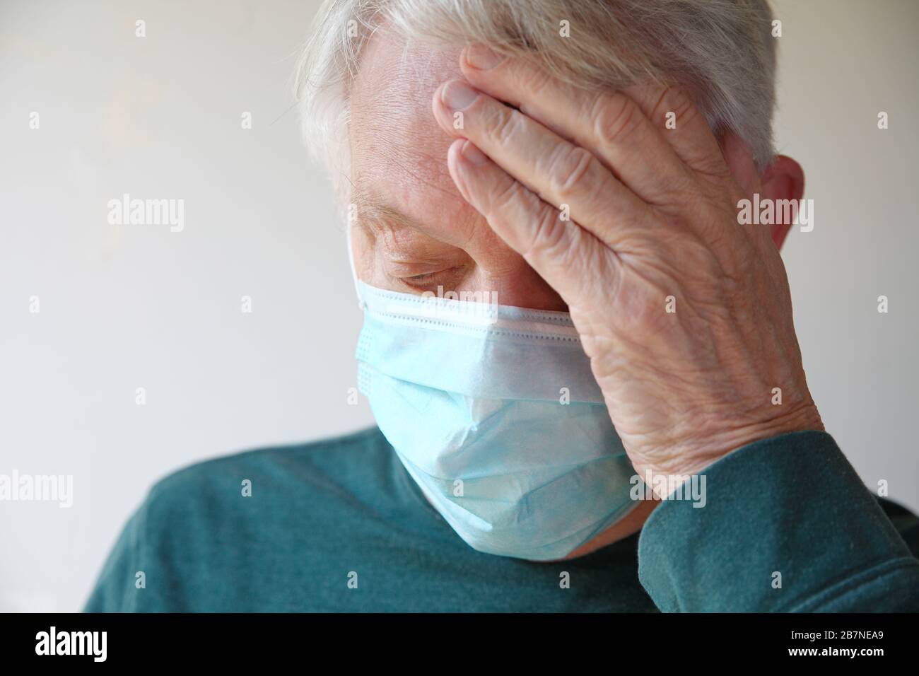 L'homme senior porte un masque facial et tient une main à sa tête Banque D'Images
