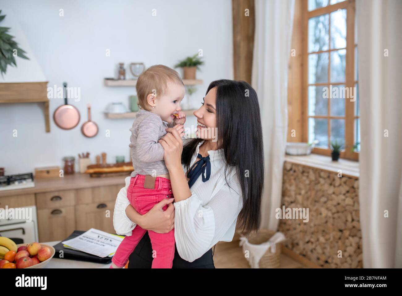 Jeune maman tenant la fille dans les bras, fille manger biscuit Banque D'Images