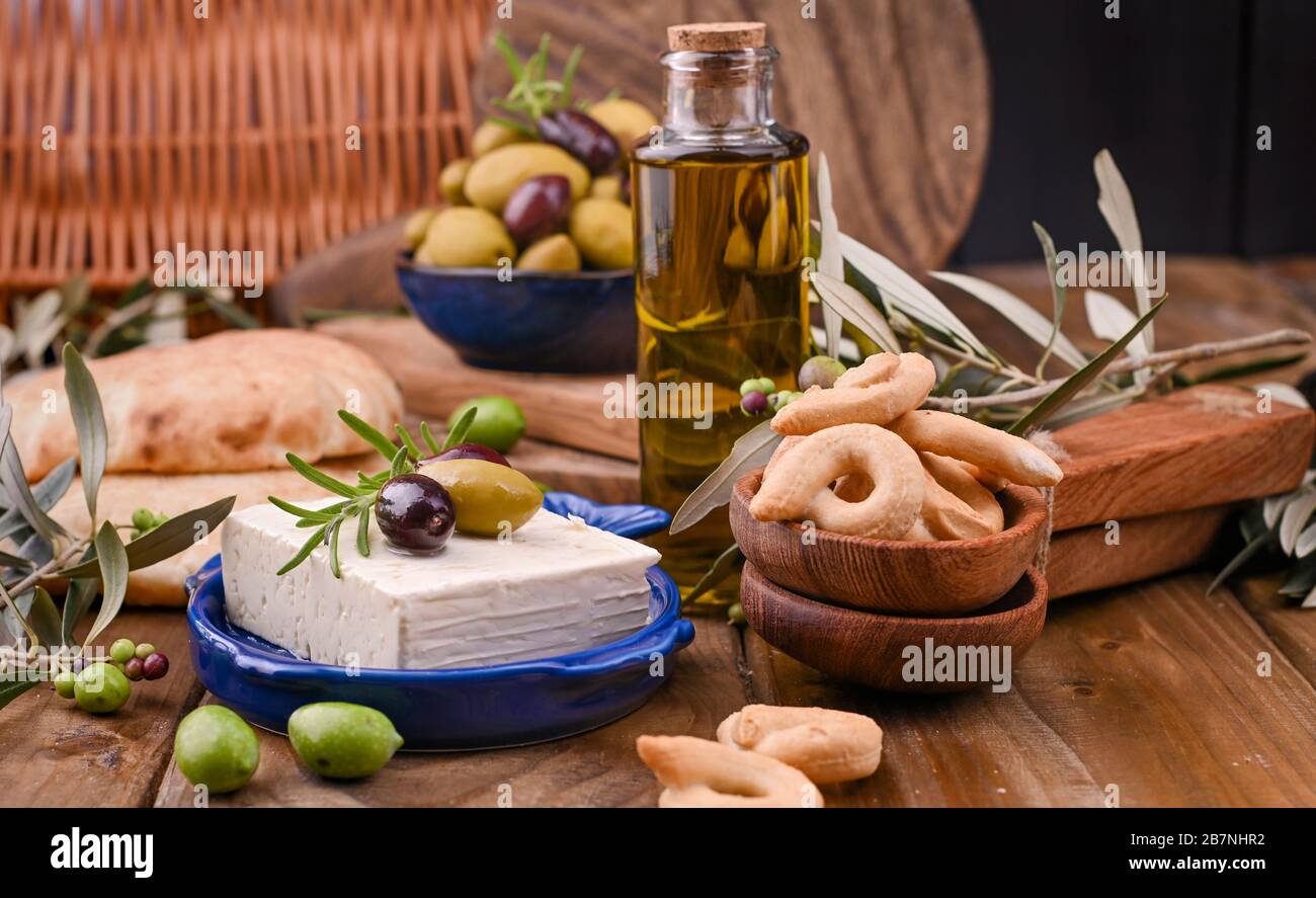 Fromage grec aux olives et CRAQUELINS italiens et ITALIENS ou TARALLI . Branches d'olive fraîches, huile d'olive dans une bouteille avec des collations italiennes traditionnelles. Espace de copie. Bannière Banque D'Images