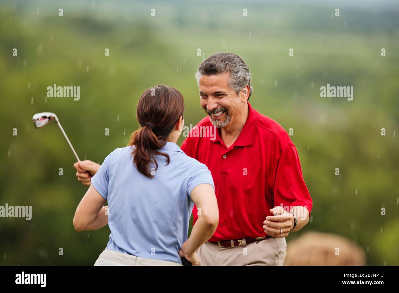 Heureux couple mûr rire ensemble car ils sont pris dans une douche de pluie soudaine sur le terrain de golf. Banque D'Images