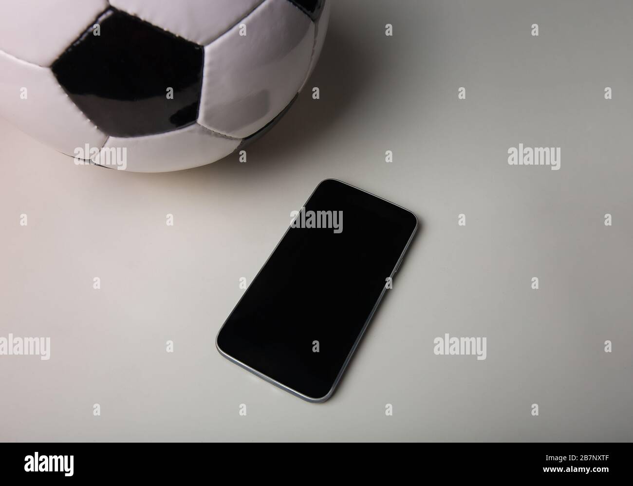 Concept de Paris de football en direct, écran vide de smartphone et ballon de football classique isolé sur fond minimaliste de table grise. Application de jeu de sport, jouer Banque D'Images