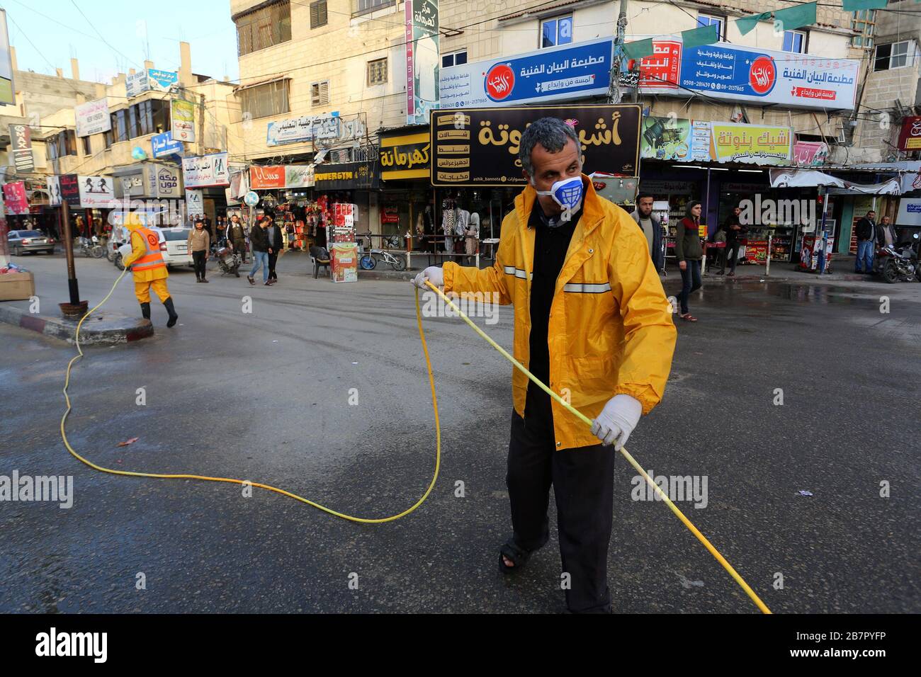 Les travailleurs de la municipalité portant des vêtements de protection désinfectent une rue de la bande de Gaza le 14 mars 2020 afin d'empêcher la propagation du Coronavirus. Banque D'Images