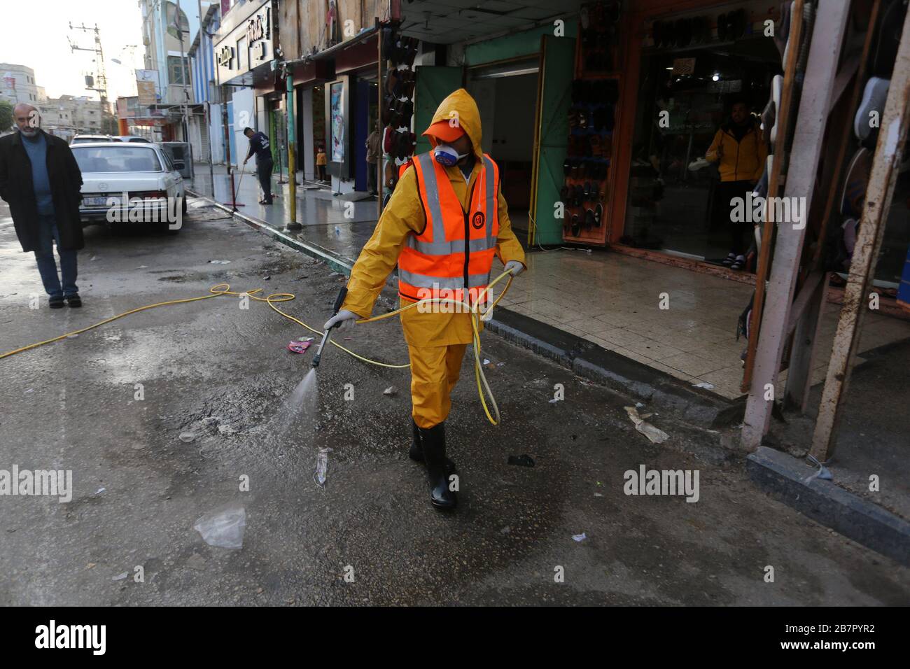Les travailleurs de la municipalité portant des vêtements de protection désinfectent une rue de la bande de Gaza le 14 mars 2020 afin d'empêcher la propagation du Coronavirus. Banque D'Images