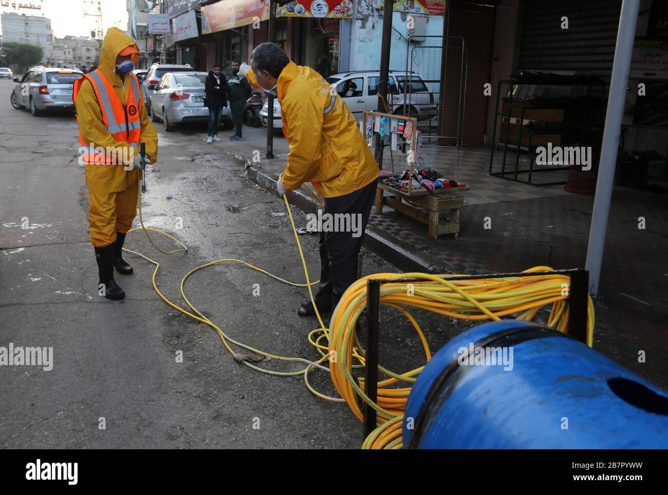 Les travailleurs de la municipalité portant des vêtements de protection désinfectent une rue de la bande de Gaza le 14 mars 2020 afin d'empêcher la propagation du Coronavirus. Banque D'Images