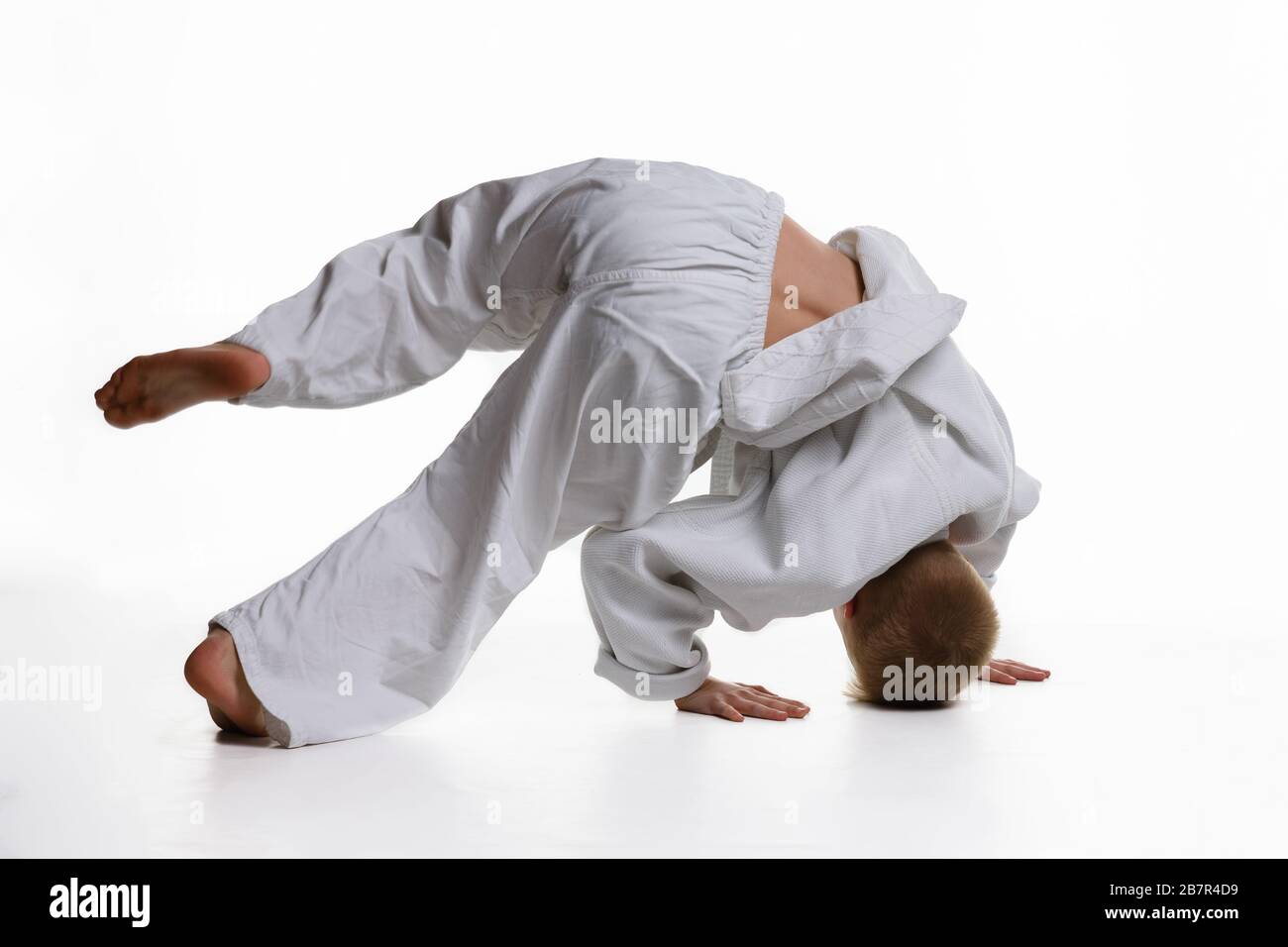 Judo garçon qui fait de l'échauffement se tournoyant autour de lui tout en se tenant sur sa tête Banque D'Images